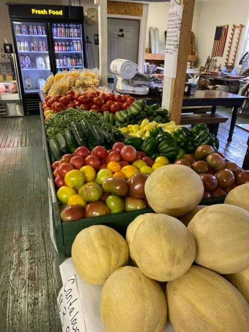 A vibrant display of fresh fruits and vegetables, including melons, apples, peppers, and cucumbers, in a market setting.