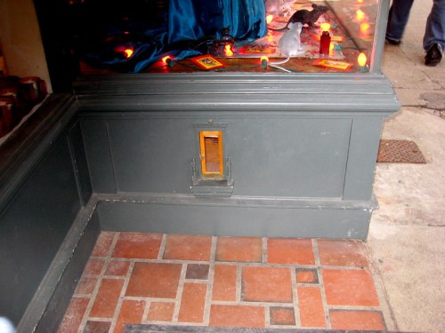 A small, rectangular opening in a gray wall, with a wooden frame, set against a brick floor.