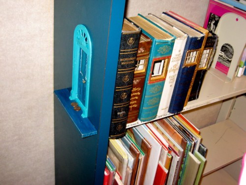 A bookshelf with colorful books and a small blue door decoration on the side.