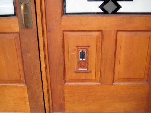Close-up of a wooden door with a decorative panel and a vintage-style doorbell or intercom.