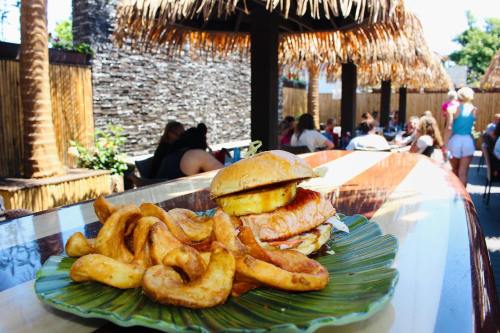 A burger with pineapple and crispy fries on a green plate, with a lively outdoor dining area in the background.