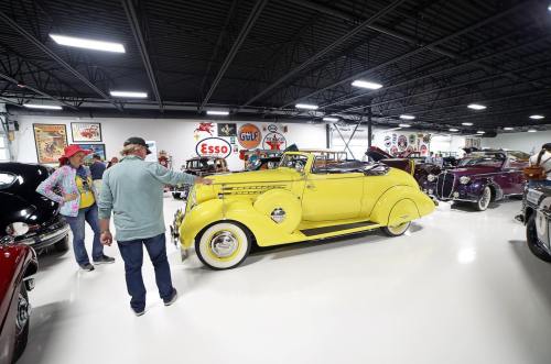 A vintage car show featuring a bright yellow convertible and various classic cars in a well-lit garage.