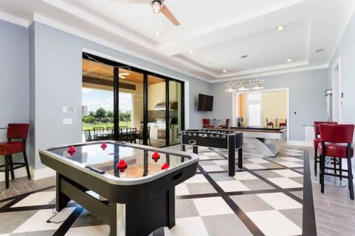 A spacious game room featuring air hockey and foosball tables, with large windows and modern decor.