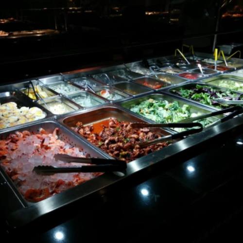 A buffet display featuring various dishes, including seafood, salads, and sauces, in metal trays.