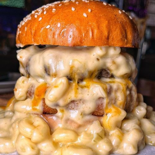 A towering burger topped with creamy macaroni and cheese, all nestled in a sesame seed bun.