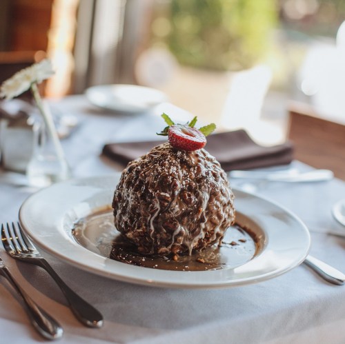 A decadent chocolate dessert topped with a strawberry and mint, served on a white plate with a rich sauce.
