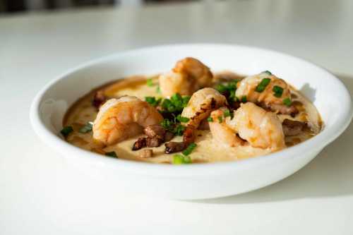 A bowl of creamy shrimp and grits topped with green onions and pieces of bacon.