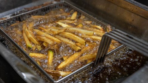 Golden French fries frying in a basket, bubbling in hot oil.