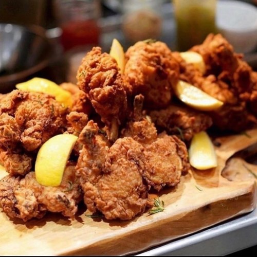 A platter of crispy fried chicken pieces garnished with lemon wedges on a wooden board.