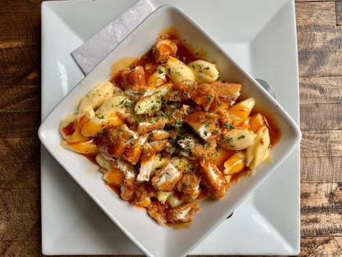 A bowl of pasta topped with shredded chicken, marinara sauce, and herbs, served on a wooden table.