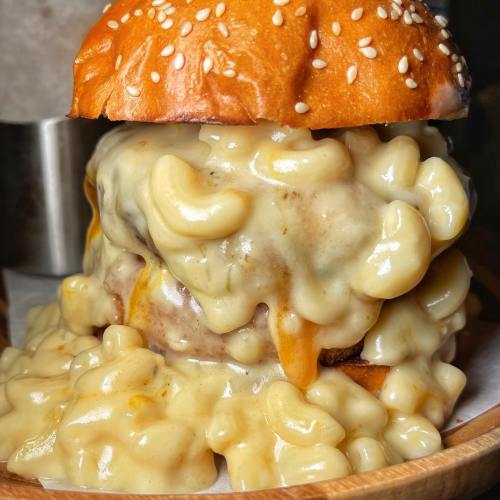 A close-up of a sesame seed burger overflowing with creamy macaroni and cheese.