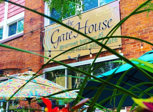 A colorful sign for "The Gate House" restaurant, surrounded by greenery and vibrant umbrellas.
