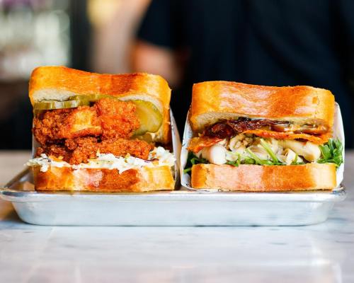Two delicious sandwiches on a tray: one with fried chicken and pickles, the other with turkey and greens.