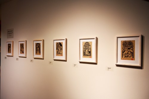 A gallery wall displaying six framed artworks with labels beneath each piece.