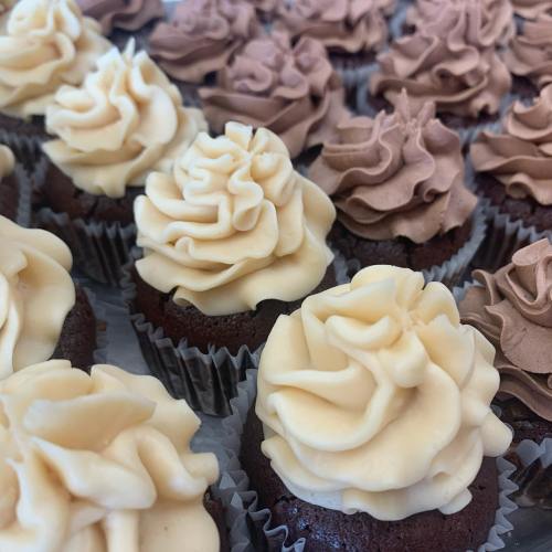 A close-up of chocolate cupcakes topped with swirls of yellow and brown frosting, arranged neatly in paper liners.