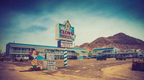 Sign for the Clown Motel with colorful buildings and mountains in the background, featuring a clown-themed design.