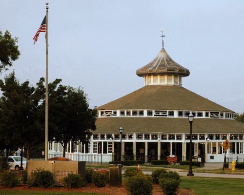 A round building with a conical roof, surrounded by trees, with an American flag and a lamp post in the foreground.