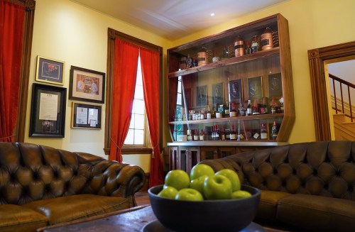 A cozy room with leather sofas, red curtains, and a wooden shelf displaying various bottles and framed artwork.