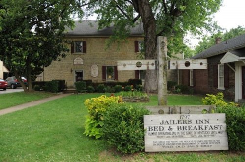 Historic Jailer's Inn Bed & Breakfast with a wooden sign and lush greenery in front of a stone building.