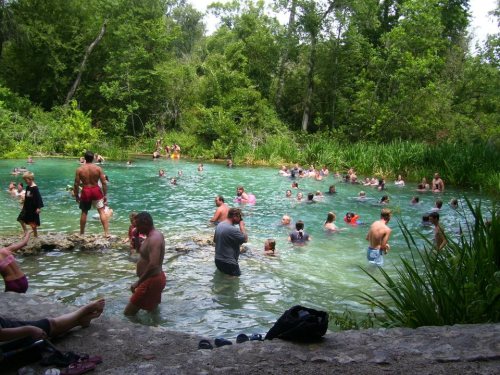 A crowded natural swimming area with people enjoying the water surrounded by lush greenery.