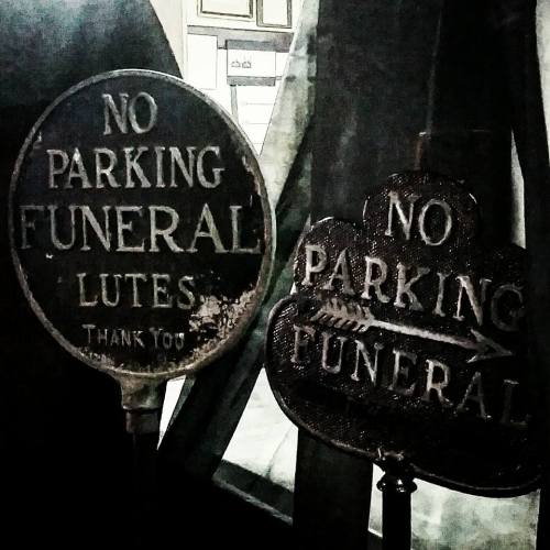 Two vintage signs reading "No Parking Funeral" and "No Parking Funeral Lutes Thank You," set against a dark background.