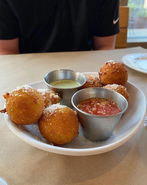 A plate of golden-brown fried balls with two dipping sauces, one creamy and one red, on a table.