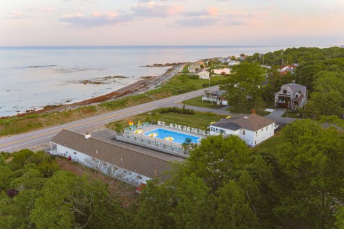 Aerial view of a coastal area with a pool, houses, and a road along the shoreline at sunset.