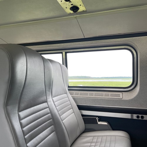 Interior view of a train with two empty gray seats and a window showing a green landscape outside.