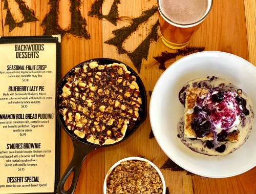 A table with a dessert menu and three desserts: fruit crisp, blueberry pie, and cinnamon roll bread pudding with ice cream.