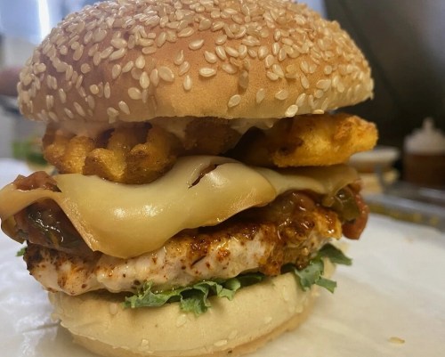 A close-up of a sesame seed burger with chicken, melted cheese, lettuce, and crispy potato wedges inside.