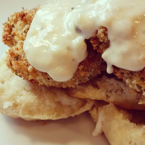 A close-up of a biscuit topped with crispy fried chicken and creamy white gravy.