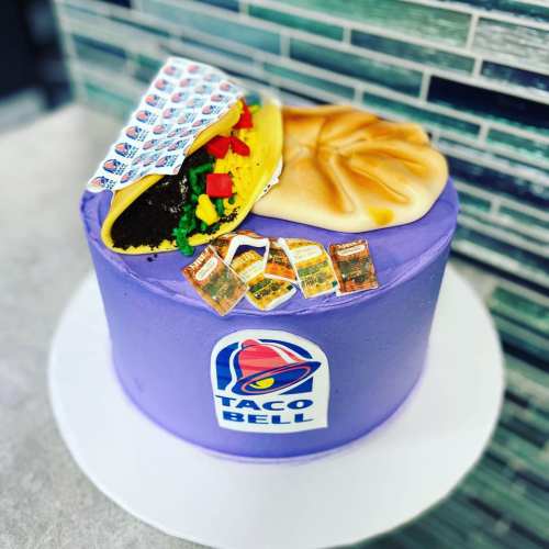 A colorful cake decorated to resemble Taco Bell items, featuring a taco and sauce packets on top.