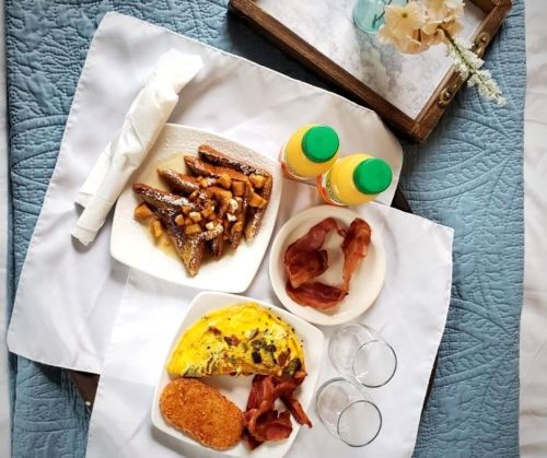 A breakfast tray with French toast, bacon, an omelet, and orange juice on a white tablecloth.