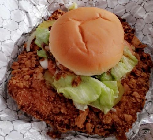 A fried chicken sandwich with lettuce on a bun, resting on a bed of crispy fried chicken pieces.
