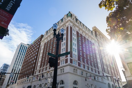 Historic building with ornate architecture, sunlight shining from the corner, surrounded by modern skyscrapers.