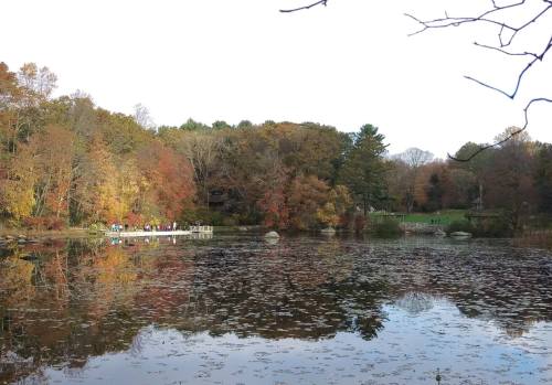 A serene lake surrounded by autumn trees, reflecting colorful foliage and a small group of people on a dock.