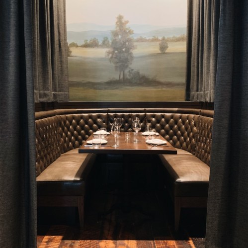 Cozy restaurant booth with a wooden table, elegant glassware, and a scenic mural in the background.