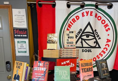 A cozy bookstore display featuring books, a sign about sanitization, and a colorful banner with an eye symbol.