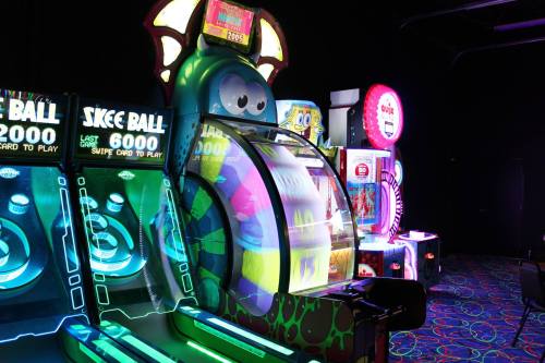 Brightly lit arcade with skee ball machines and colorful game displays in a dark room.