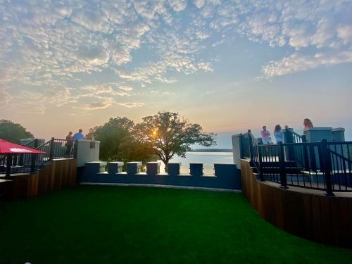 A scenic view of a sunset over water, with people enjoying the outdoors on a terrace surrounded by greenery.