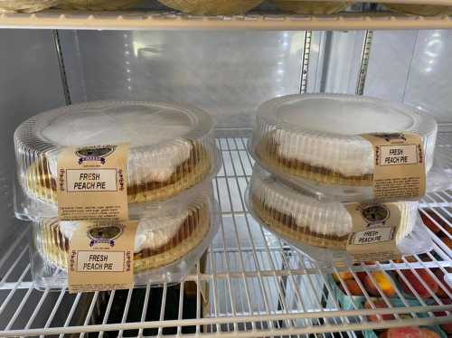 Four fresh peach pies in clear plastic containers on a refrigerator shelf.