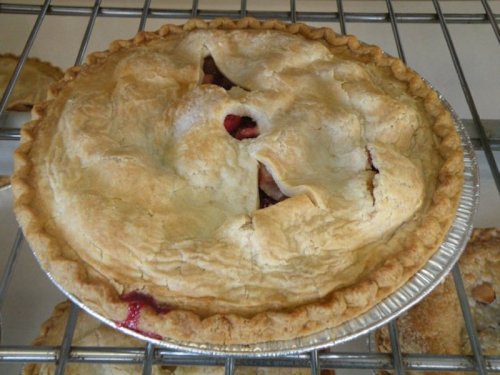 A golden-brown pie with a flaky crust, featuring a small opening on top, resting on a wire rack.