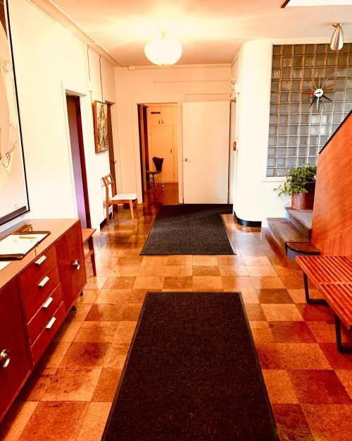 A hallway with wooden furniture, a staircase, and two doorways, featuring a patterned floor and potted plants.