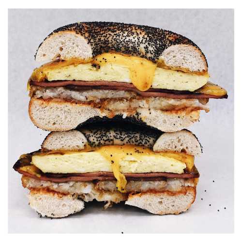 A stacked bagel sandwich with poppy seed bagels, layers of ham, egg, and melted cheese.