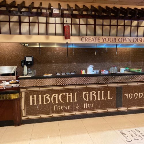 Interior of a hibachi grill restaurant featuring a counter with "Hibachi Grill" signage and a create-your-own-dish setup.