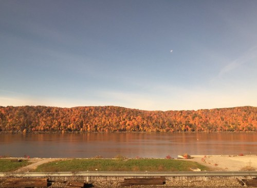A serene river scene with vibrant autumn foliage reflecting on the water under a clear sky.