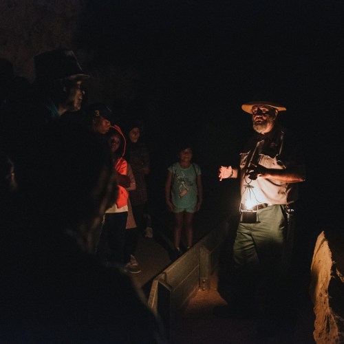 A park ranger speaks to a group of visitors inside a dimly lit cave.