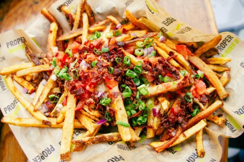 A large serving of loaded fries topped with bacon, green onions, and diced tomatoes in a paper-lined basket.