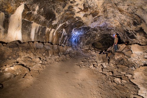 A person stands in a rocky cave, illuminated by a flashlight, showcasing the textured walls and uneven ground.