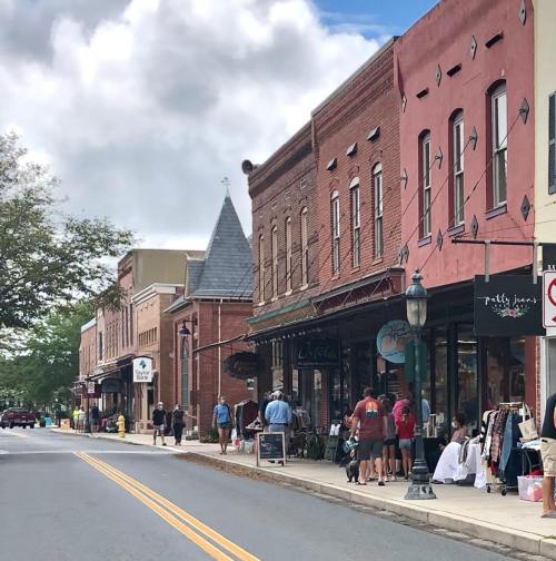 A charming street lined with historic brick buildings, shops, and people enjoying a sunny day.